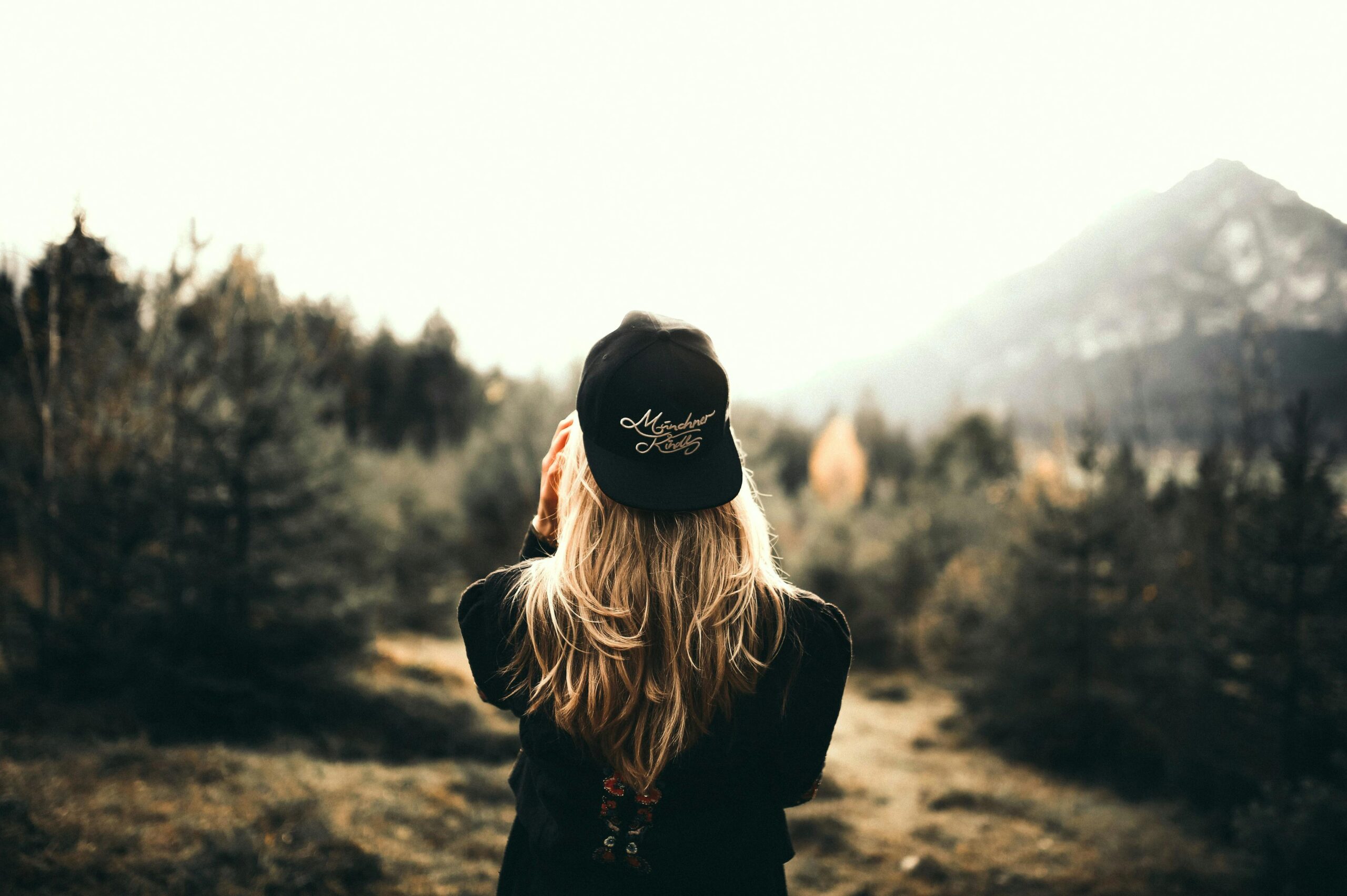 A woman in black cap and sweater enjoys a mountain view, embracing outdoor adventure.