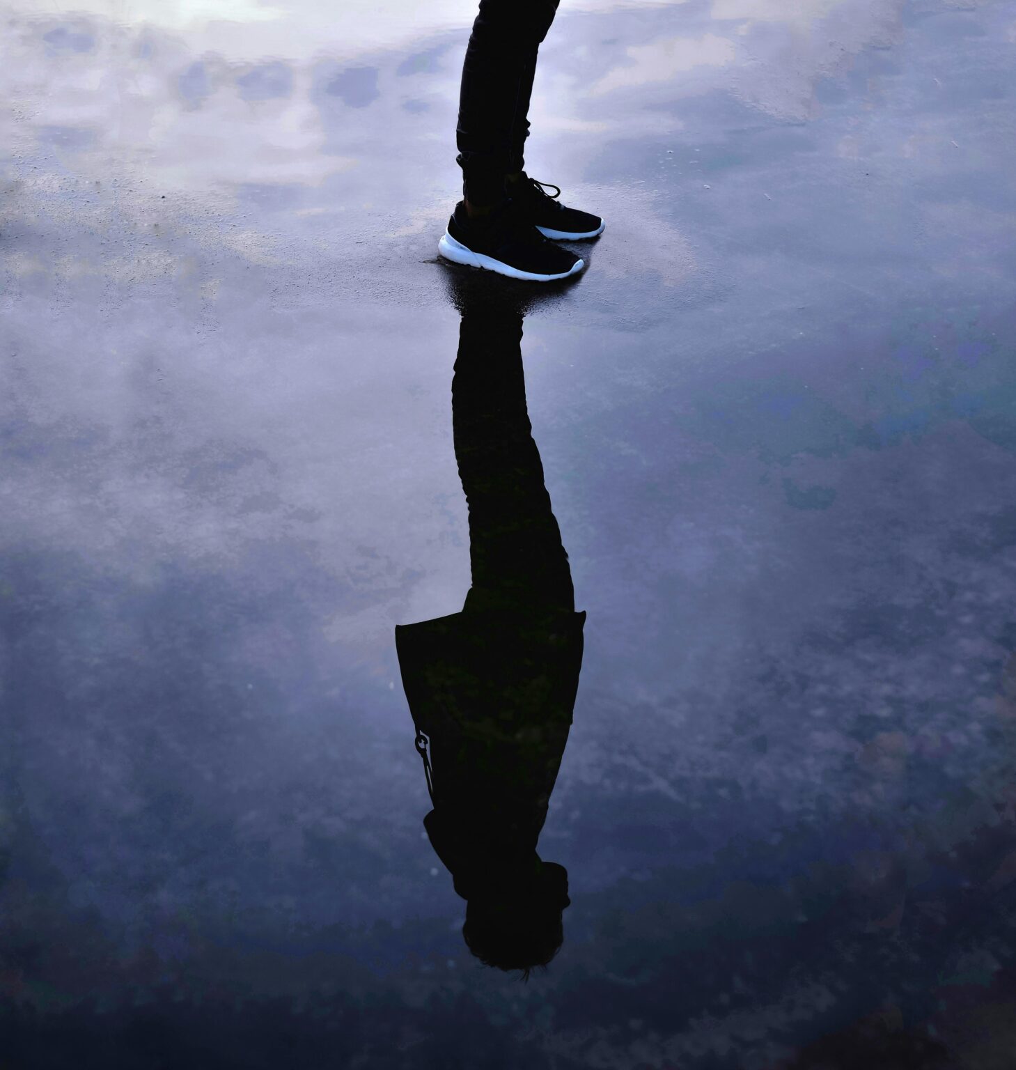 A person stands on wet ground with a clear reflection in water, showcasing sneakers.